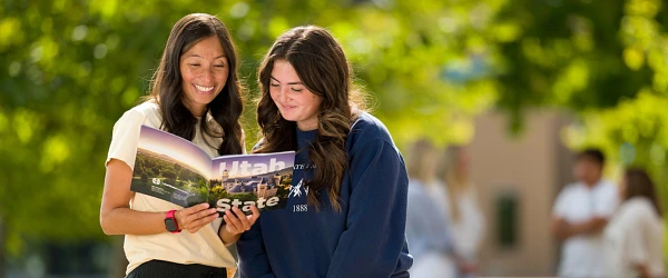 Two people are happily reading a Utah State University brochure outdoors.